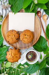 Muffins and cup of herbal tea with blank card, wooden plate, wooden spoon and season herbs on cotton tablecloth.card. Template for recipes or food menu