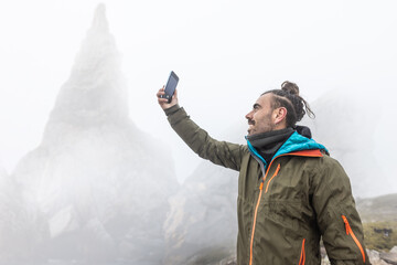 man on the mountain in the fog with rain, wet, long hair looking for cover with cell phone, wild...