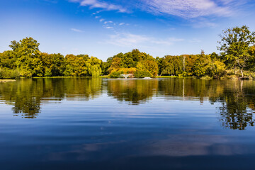 Beautiful sunny panorama of big lake with small fountains at center and green trees and bushes around in city South park