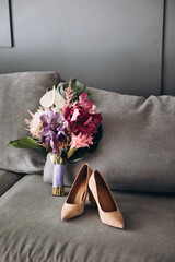 Wedding Details. A bouquet of bright flowers and greenery with a ribbon and heeled shoes standing on the couch
