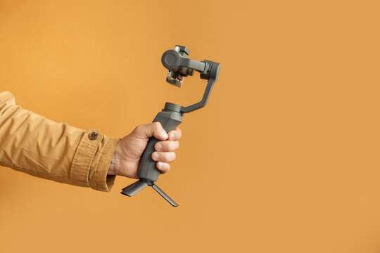 Man hand filming with a smartphone using a gimbal stabilizer on yellow background. Using three-axis electronic stabilizer to make vlogs or video shooting. Copy space for a free text