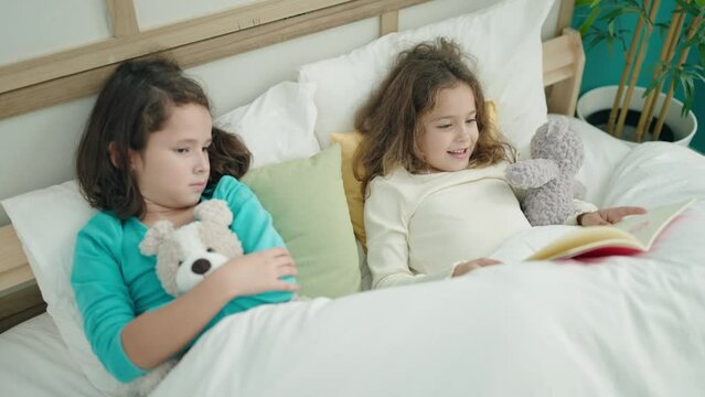 Adorable girls reading book lying on bed at bedroom