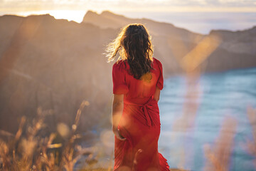 Back view of woman in red dress walking down a hill in the morning on a volcanic island in the...