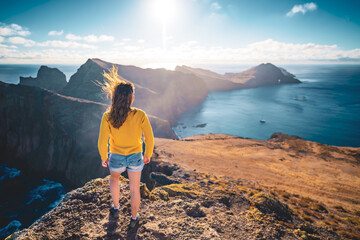 Fototapeta premium Back view of a woman looking at the foothills of a volcanic island in the Atlantic Ocean from a panoramic morning viewpoint. São Lourenço, Madeira Island, Portugal, Europe.