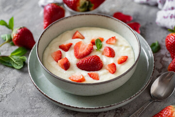Delicious breakfast for children: sweet milk semolina porridge with strawberries on a beautiful plate on a gray background, strawberries on a gray background. Semolina porridge with milk for lunch for