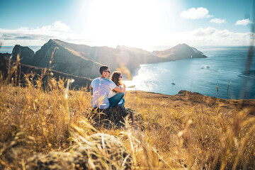 Back view of a tourist couple sitting on a hillside, overlooking the coastal landscape of Madeira...