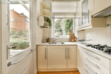 a kitchen with wood flooring and white cabinetd cupboards on either side of the window looking out onto the street