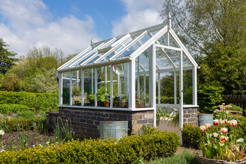 A garden plot with seedbeds and a glass greenhouse in the center of kitchen garden. A suburban or rustic backyard for gardening. A warm summers day.Trentham gardens staffordshire