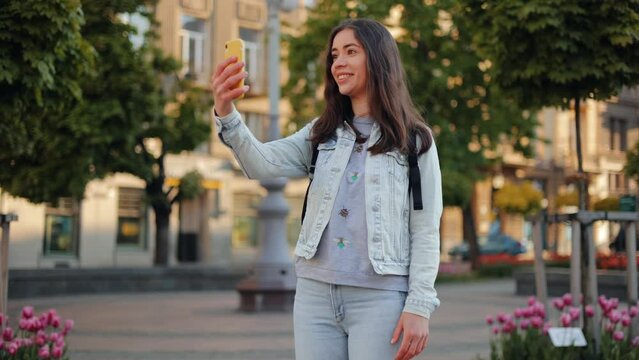 A young smiling attractive girl is talking to a friend using a smartphone while on a trip walking down the street of Lviv city. in slow motion.