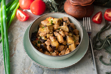 A hearty lunch for the family. A dish for dinner. Eggplant stewed with pork, spices and vegetables in a beautiful plate on a gray background. Close-up.
