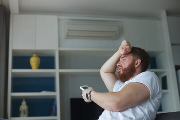 Young man with air conditioner remote control using air conditioner at home, guy is cooling off...