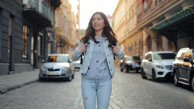 A young smiling woman walks down a city street. A beautiful tourist girl smiles against the city background, looks around and admires the architecture of the city of Lviv
