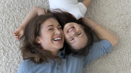 Cheerful loving young mom caressing cute little kid girl with face touch, lying on heating floor, soft carpet, hugging child, smiling, laughing, enjoying motherhood, family funny leisure time