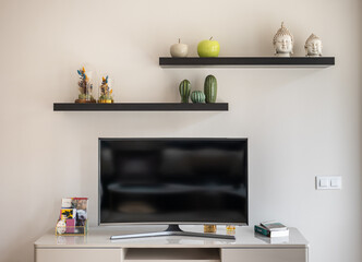 Close-up of a home theater tv on a white wall with shelves and stylish interior accessories. The concept of living room for a young family or hotel. Copyspace