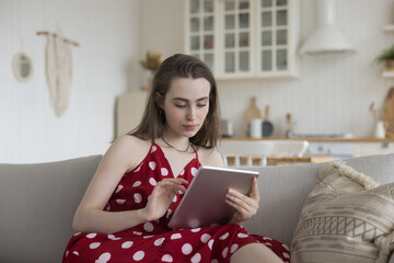 Focused beautiful young adult girl using modern technology, Internet application on tablet,...