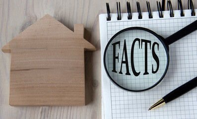 The word FACTS under a magnifying glass on a white notebook against the background of a wooden house and banknotes
