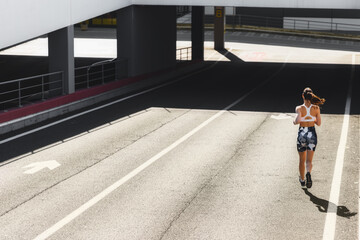 Back view of a young woman runner in sportswear running on sunny morning on city. Healthy lifestyle concept. Copy space