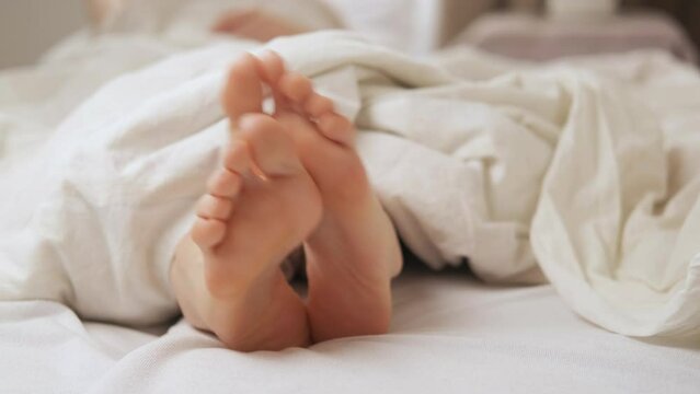 Women's feet itch in bed under a white blanket. Foot diseases, fungus