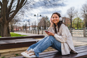 One young girl is listening to music on her wireless headphones and using her phone outdoors