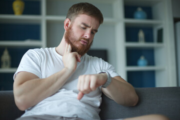  Tired man measuring, checking heart rate pulse with fingers on his neck and looking sport watch at...