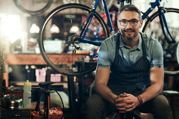 Fototapeta na wymiar Portrait, smile and technician man in bicycle shop, store or cycling repair workshop. Face, bike mechanic and male person, confident business owner or mature professional from Canada with glasses.