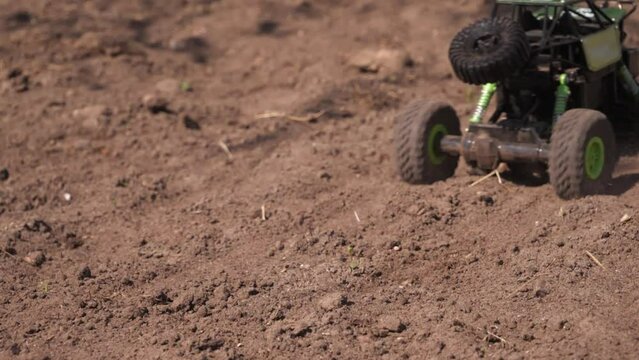 A radio-controlled toy car starts on the sand. The wheels of the toy car spin and sand and dust fly from them. Slow motion video. Radio-controlled buggy car drives off-road.