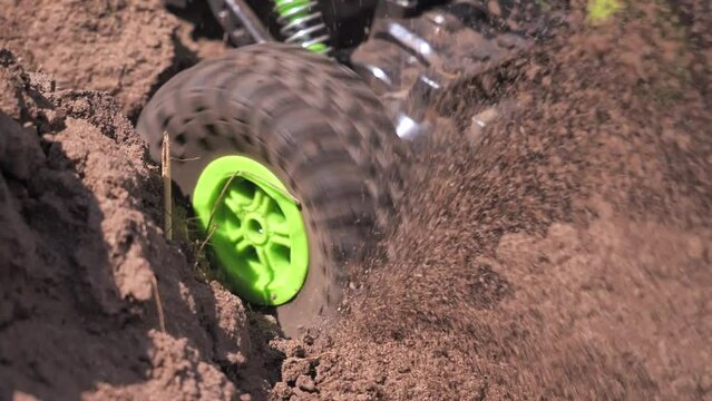 Close-up of the wheel of a toy radio-controlled car spinning in dry ground. Sand and dust fly out beautifully in slow motion from under the wheels of a toy car. The concept of children's toys.