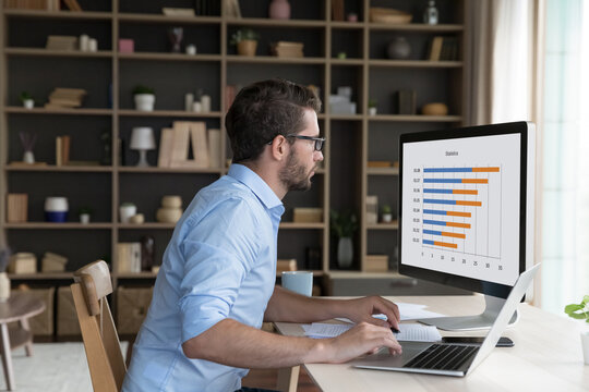 Serious young freelancer man analyzing business diagram, marketing statistics on desktop monitor. Broker, investor studying project data charts, rates, using job application for strategy analysis - Powered by Adobe
