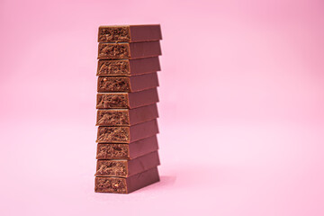 Broken milk chocolate on pink background.