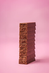 Broken milk chocolate on pink background.