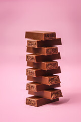 Broken milk chocolate on pink background.