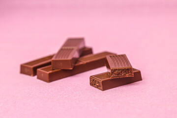 Broken milk chocolate on pink background.