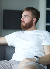 Portrait young european beard pensive thoughtful relaxed lonely guy, man is dreaming, thinking, relax at home in living room at comfortable sofa, couch with his hands behind head 