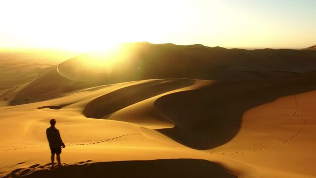 Travel, desert and silhouette of man at sunset with drone for destination, freedom or summer trip. Footprints, adventure and journey with guy on horizon of sand dunes on trip of Namibia vacation