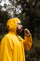 portrait of a man in a bright yellow raincoat with hood in the middle of the forest calling the dog with an ultrasonic whistle in the middle of the rain.