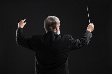 Professional conductor with baton on black background, back view © New Africa