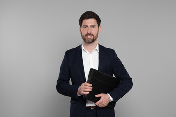 Happy real estate agent with leather portfolio on grey background