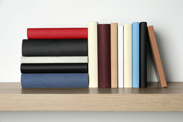 Many hardcover books on wooden shelf near white wall