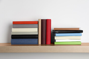 Many hardcover books on wooden shelf near white wall
