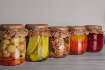 Many jars with preserved vegetables on white wooden table