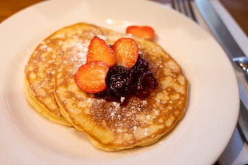 Homemade American pancakes served with strawberry jam and fresh ripe strawberries on a white board, sweet dessert