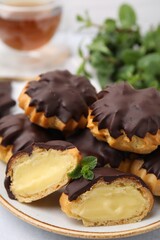 Delicious profiteroles with chocolate spread and cream on plate, closeup