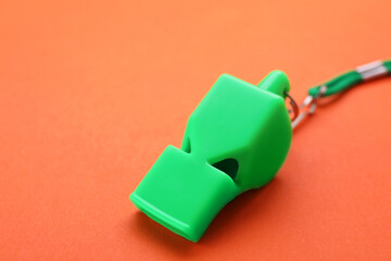 One green whistle with cord on orange background, closeup