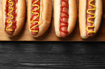 Delicious hot dogs with mustard and ketchup on black wooden table, top view. Space for text