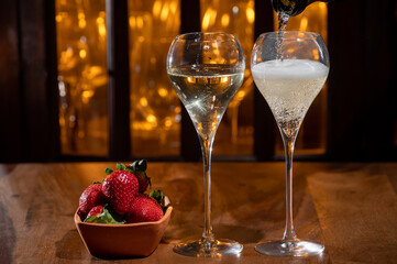 Glass of brut champagne bubbles wine in tulip glass and bowl with fresh strawberries on evening bar...