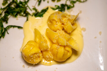 Italian food, fresh home made pumpkin stuffed pasta tortellini or ravioli dumplings with parmesan parmigiano reggiano cheese sauce with dried rocket salad