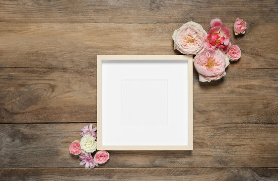 Empty photo frame and beautiful flowers on wooden table, flat lay. Space for design