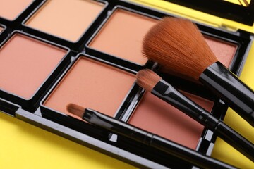 Colorful contouring palette with brushes on yellow background, closeup. Professional cosmetic product