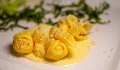 Italian food, fresh home made pumpkin stuffed pasta tortellini or ravioli dumplings with parmesan parmigiano reggiano cheese sauce with dried rocket salad