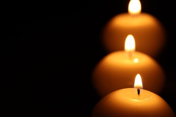 Burning wax candles on black background, closeup. Space for text